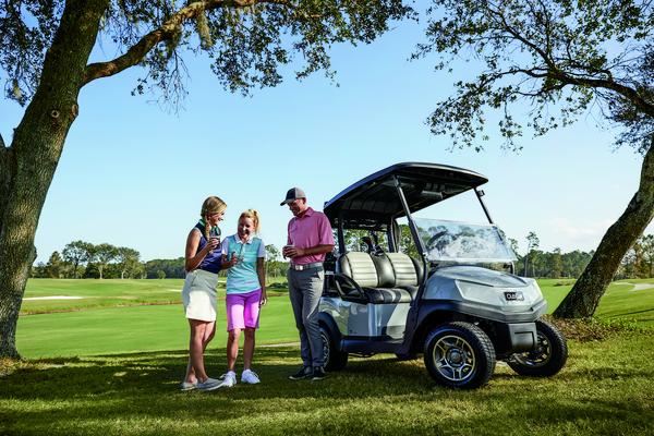 Tre golfspillere står foran en golfvogn på en golfbane og diskuterer spillet.